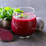 Ein Glas tiefroter Rote Bete Saft, garniert mit Minze, neben frischen Rote Bete Knollen und Scheiben. Ein natürlicher Booster für Vitalität und eine gesunde Erektion.