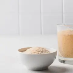 Ein Glas mit Flohsamenschalen-Getränk wird gerührt. Daneben eine Schale mit trockenen Flohsamenschalen. Frage: wie viel Flohsamenschalen am Tag?