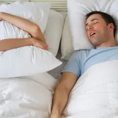 Mann schnarcht laut, Frau hält sich Kissen vors Gesicht. Mögliche schlafapnoe symptome.