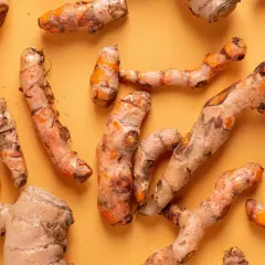 Frische Kurkumawurzeln, bekannt für ihre entzündungshemmende Kurkuma Wirkung, liegen auf einem orangefarbenen Hintergrund.