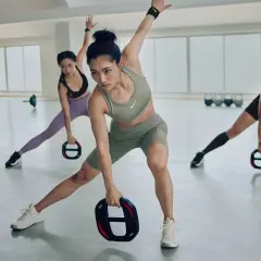 Drei Frauen in Sportkleidung trainieren in einer hellen Halle. Sie halten Gewichte und machen Ausfallschritte, um ihre aerobe Zone zu aktivieren.