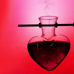 Herzförmige Glasflasche mit dampfender Flüssigkeit, die an ein Liebestrank-Experiment erinnert. Was ist Aphrodisiakum?