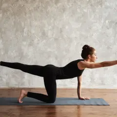 Frau in Yoga-Pose "Bird Dog" auf einer Matte, streckt Arm und Bein aus.