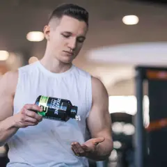 Ein Mann im Fitnessstudio schüttet Kreatin-Kapseln aus einer Flasche in seine Hand. Vielleicht zu viel Kreatin?