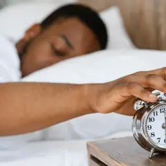 Ein Mann schaltet den Wecker aus. Warum kriegt man eine Morgenlatte? Vielleicht wegen des erholsamen Schlafs, der hier angedeutet wird.