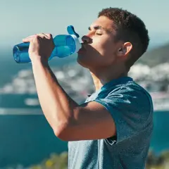 Ein Mann trinkt aus einer blauen Flasche, genießt die Aussicht und das warme Wasser.