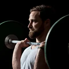 Ein Mann mit Bart hebt eine Langhantel. Er fragt sich, wie oft Krafttraining optimal ist.