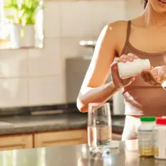 Frau nimmt Kapseln ein, die ein biologisch wichtiges Spurenelement enthalten. Daneben stehen Flaschen mit Nahrungsergänzungsmitteln und ein Glas Wasser.