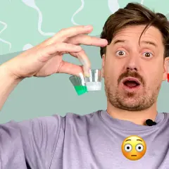 Mann mit überraschtem Gesicht hält kleine Becher mit bunten Flüssigkeiten. Er fragt sich, ob Sperma komisch riecht.