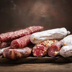 Ein Haufen verschiedener Salamisorten, von denen einige mit Gewürzen bedeckt sind. Die Frage, ob **ist schweinefleisch ungesund**, bleibt bei dieser appetitlichen Auswahl offen.