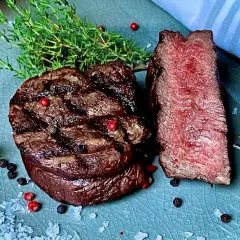 Perfekt gegrilltes Rinderfilet mit zarten rosa Kern, garniert mit frischem Thymian und bunten Pfefferkörnern. Ein Genuss für jeden Fleischliebhaber.