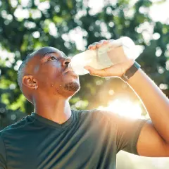 Mann trinkt nach dem Sport aus einer Flasche. Sind Elektrolyte gesund? Ja, sie helfen, den Körper nach Anstrengung zu rehydrieren.