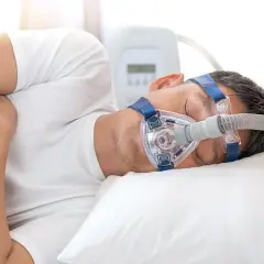 Mann schläft mit CPAP-Maske, um Atemaussetzer am Tag zu behandeln. Ein Gerät unterstützt die Atmung im Schlaf.