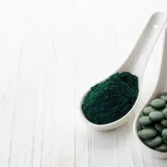 Zwei Löffel mit Spirulinapulver und Tabletten. Die Spirulina Wirkung ist vielfältig, von Energie bis zur Entgiftung.