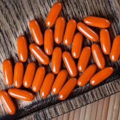 Orange Kapseln mit Beta-Carotin liegen auf einem Holzbrett. Sie könnten Rauchern helfen, ihre Lungen zu schützen.