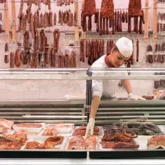 Fleischtheke mit Wurst und Fleischwaren. Eine Verkäuferin sortiert Ware. Hier findet man Inspiration, wie viel Fleisch pro Woche auf dem Teller landen könnte.