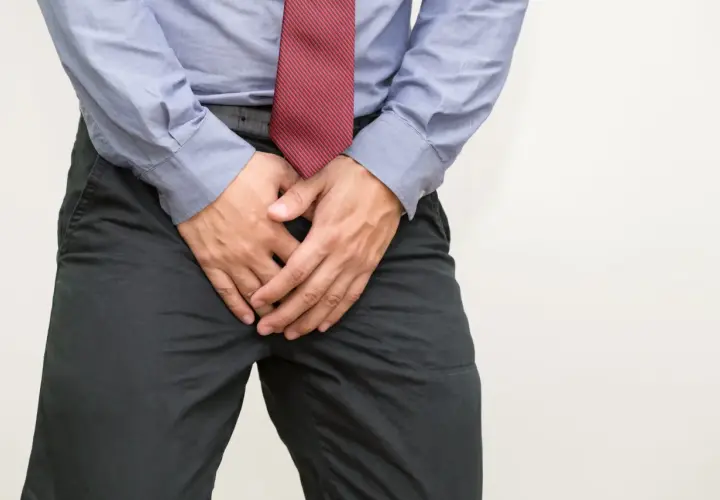 Mann mit Händen vor dem Schritt, der sich unwohl fühlt. Mögliche Ursachen für Blut im Sperma und Hausmittel.