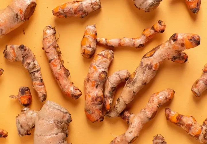 Frische Kurkumawurzeln, bekannt für ihre entzündungshemmende Kurkuma Wirkung, liegen auf einem orangefarbenen Hintergrund.