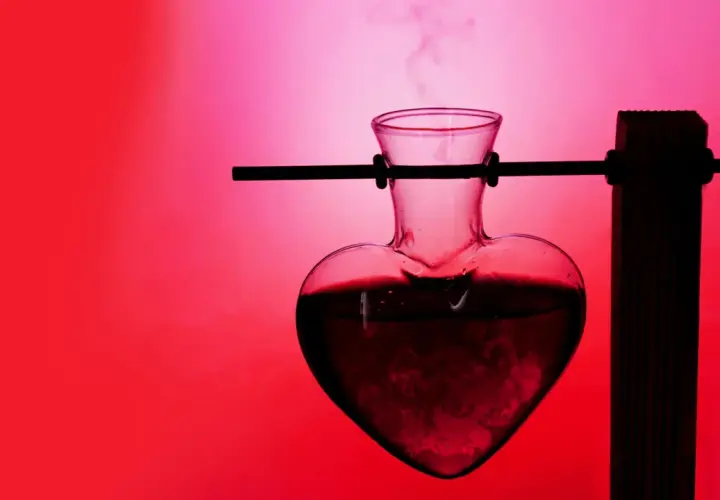 Herzförmige Glasflasche mit dampfender Flüssigkeit, die an ein Liebestrank-Experiment erinnert. Was ist Aphrodisiakum?