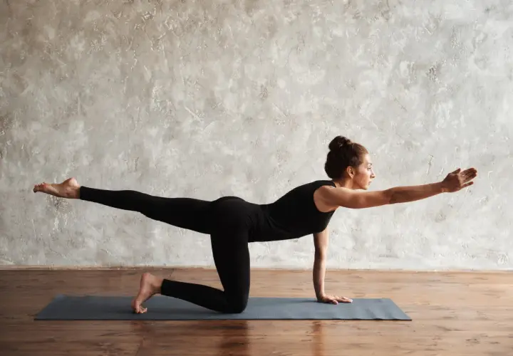 Frau in Yoga-Pose "Bird Dog" auf einer Matte, streckt Arm und Bein aus.