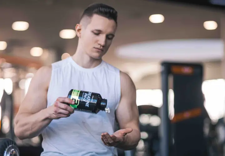 Ein Mann im Fitnessstudio schüttet Kreatin-Kapseln aus einer Flasche in seine Hand. Vielleicht zu viel Kreatin?