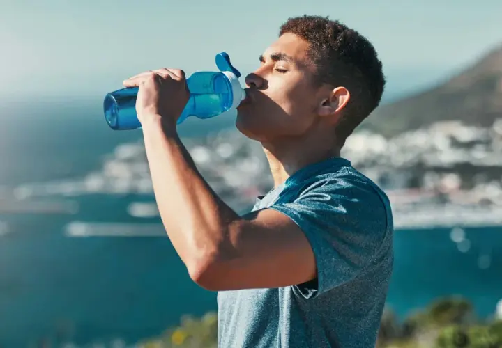 Ein Mann trinkt aus einer blauen Flasche, genießt die Aussicht und das warme Wasser.