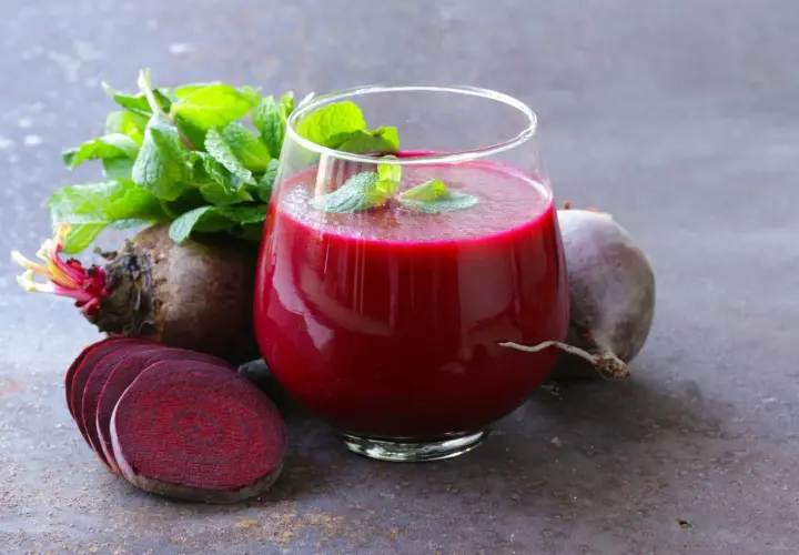 Ein Glas tiefroter Rote Bete Saft, garniert mit Minze, neben frischen Rote Bete Knollen und Scheiben. Ein natürlicher Booster für Vitalität und eine gesunde Erektion.