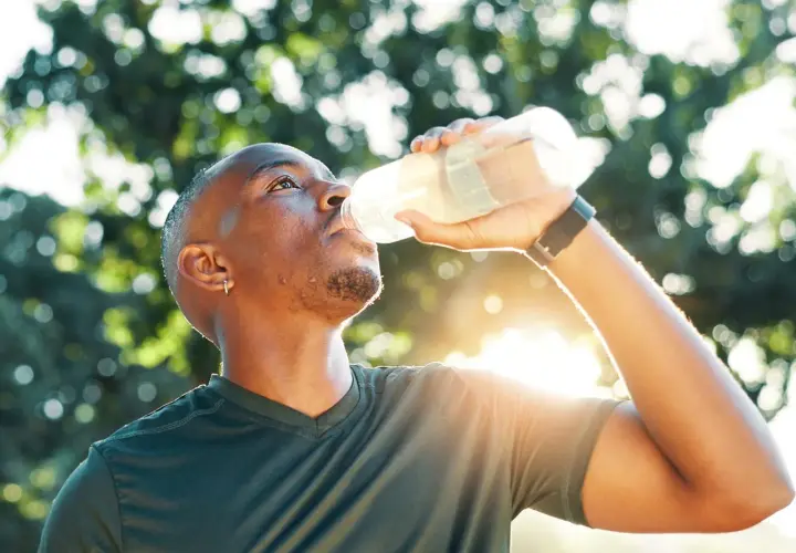 Mann trinkt nach dem Sport aus einer Flasche. Sind Elektrolyte gesund? Ja, sie helfen, den Körper nach Anstrengung zu rehydrieren.