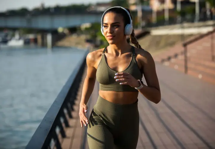 Frau mit Kopfhörern joggt am Wasser entlang. Nach 1 Monat Joggen sieht sie fit und energiegeladen aus.