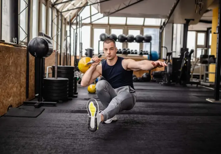 Mann macht einen Pistol Squat mit Kettlebell im Fitnessstudio.