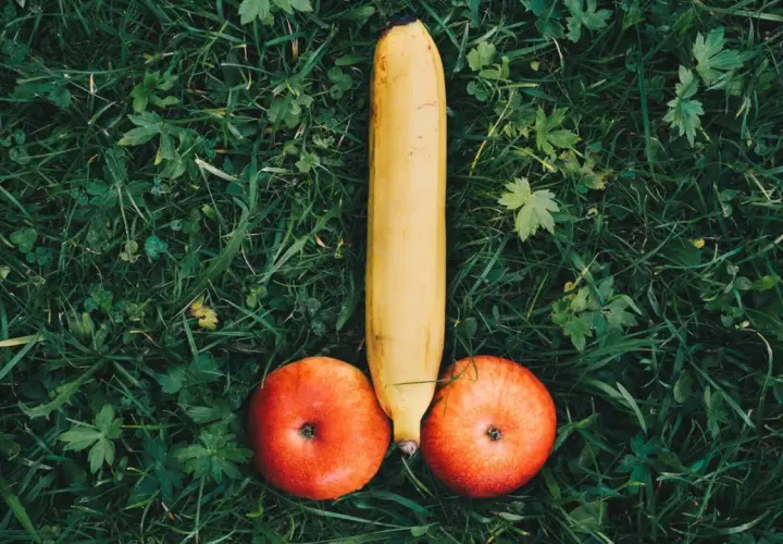 Eine Banane und zwei Äpfel liegen auf grünem Gras und bilden die Form eines kurzen dicken Penis.