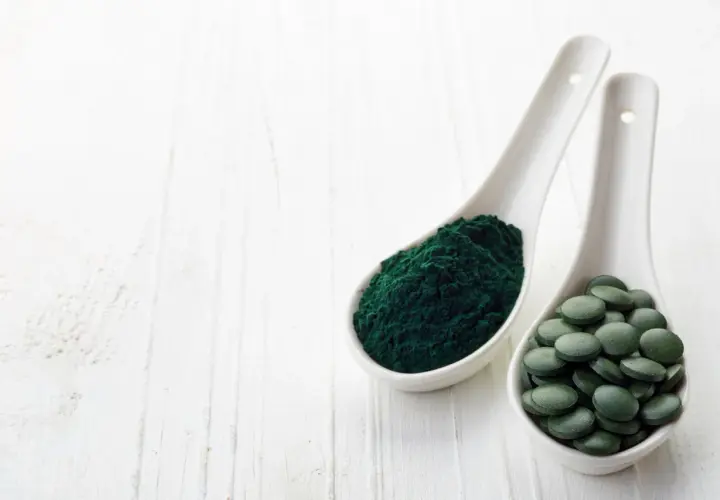 Zwei Löffel mit Spirulinapulver und Tabletten. Die Spirulina Wirkung ist vielfältig, von Energie bis zur Entgiftung.
