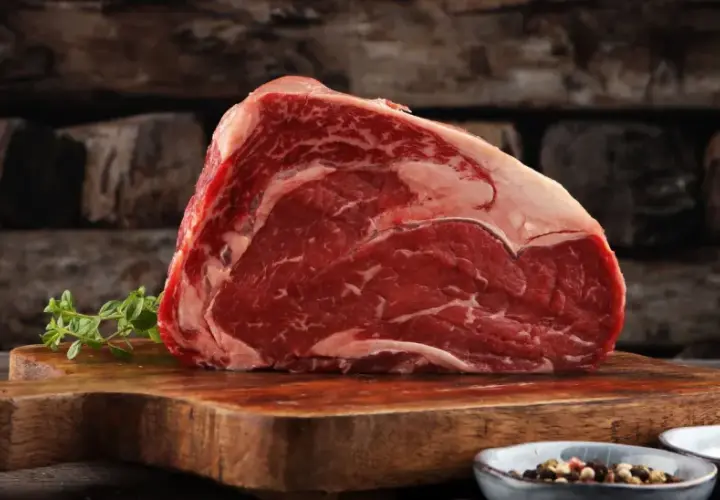 Ein saftiges Stück rotes Fleisch, reich an Eisen, liegt auf einem Holzbrett. Daneben Kräuter und Gewürze.