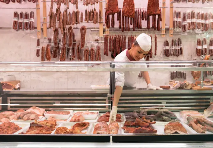 Fleischtheke mit Wurst und Fleischwaren. Eine Verkäuferin sortiert Ware. Hier findet man Inspiration, wie viel Fleisch pro Woche auf dem Teller landen könnte.