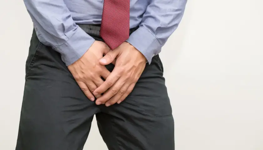 Mann mit Händen vor dem Schritt, der sich unwohl fühlt. Mögliche Ursachen für Blut im Sperma und Hausmittel.