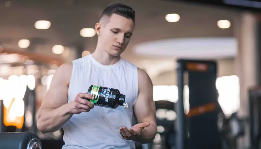 Ein Mann im Fitnessstudio schüttet Kreatin-Kapseln aus einer Flasche in seine Hand. Vielleicht zu viel Kreatin?