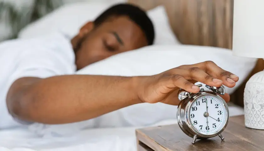 Ein Mann schaltet den Wecker aus. Warum kriegt man eine Morgenlatte? Vielleicht wegen des erholsamen Schlafs, der hier angedeutet wird.