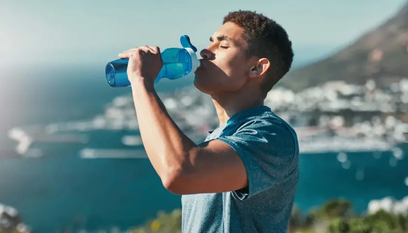 Ein Mann trinkt aus einer blauen Flasche, genießt die Aussicht und das warme Wasser.