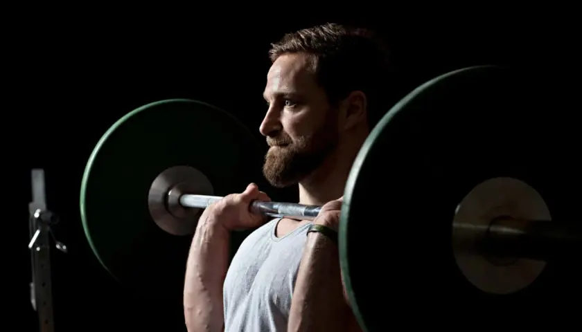 Ein Mann mit Bart hebt eine Langhantel. Er fragt sich, wie oft Krafttraining optimal ist.