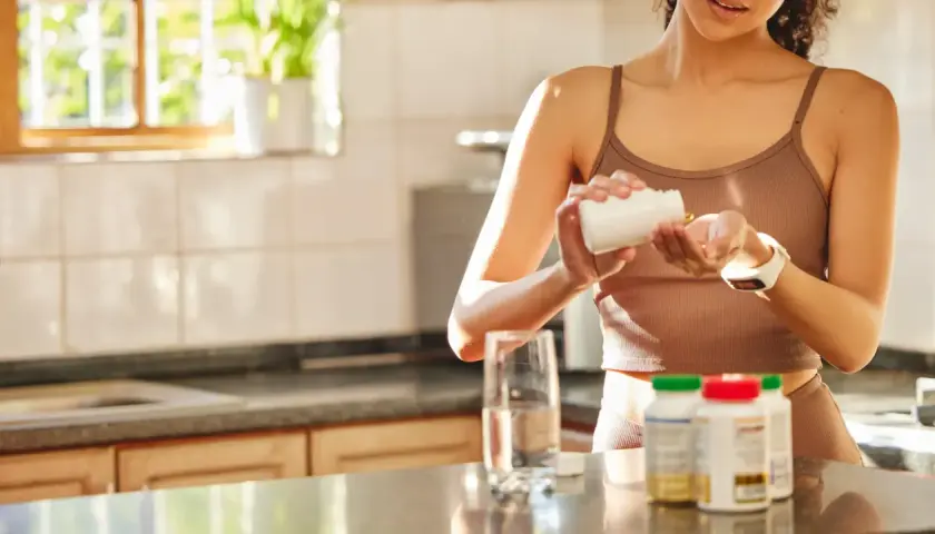 Frau nimmt Kapseln ein, die ein biologisch wichtiges Spurenelement enthalten. Daneben stehen Flaschen mit Nahrungsergänzungsmitteln und ein Glas Wasser.