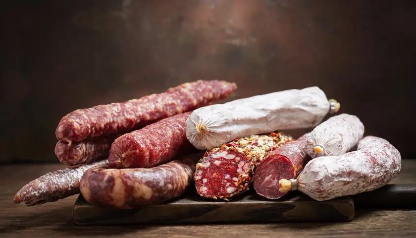 Ein Haufen verschiedener Salamisorten, von denen einige mit Gewürzen bedeckt sind. Die Frage, ob **ist schweinefleisch ungesund**, bleibt bei dieser appetitlichen Auswahl offen.