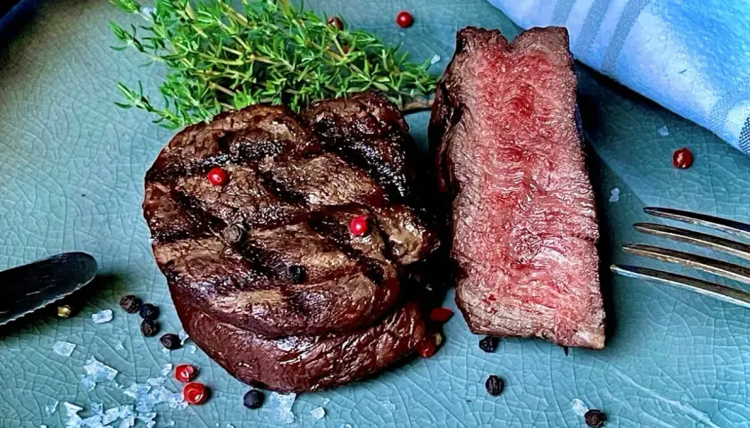 Perfekt gegrilltes Rinderfilet mit zarten rosa Kern, garniert mit frischem Thymian und bunten Pfefferkörnern. Ein Genuss für jeden Fleischliebhaber.
