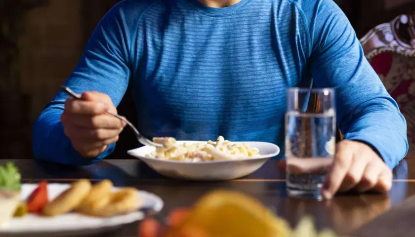 Mann isst Nudeln, um Muskelaufbau und Kohlenhydrate pro kg zu optimieren.