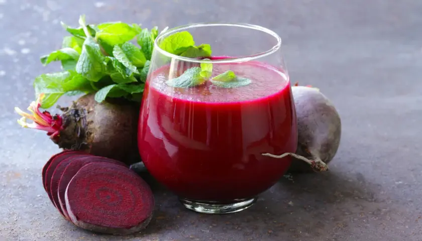 Ein Glas tiefroter Rote Bete Saft, garniert mit Minze, neben frischen Rote Bete Knollen und Scheiben. Ein natürlicher Booster für Vitalität und eine gesunde Erektion.