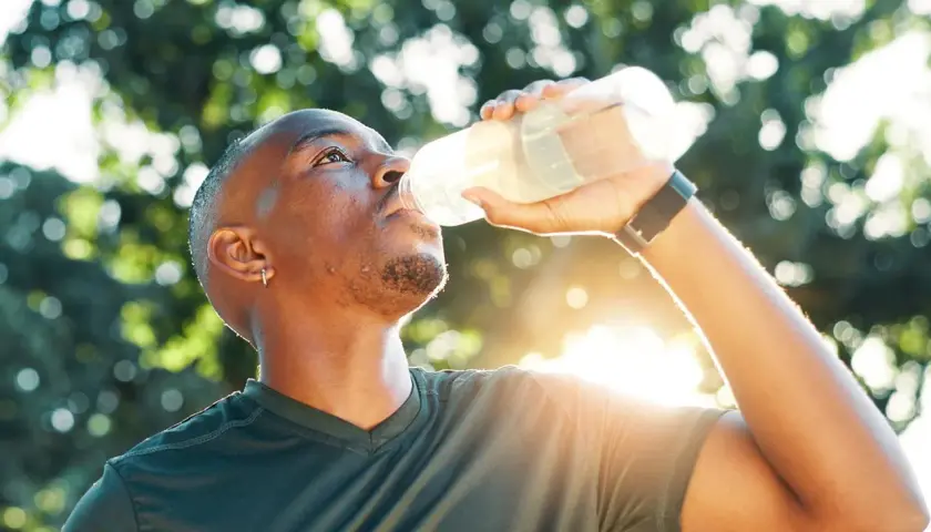 Mann trinkt nach dem Sport aus einer Flasche. Sind Elektrolyte gesund? Ja, sie helfen, den Körper nach Anstrengung zu rehydrieren.