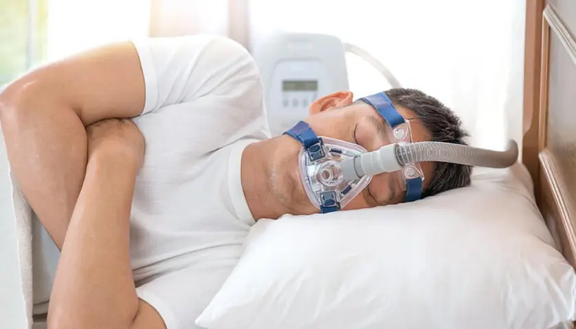 Mann schläft mit CPAP-Maske, um Atemaussetzer am Tag zu behandeln. Ein Gerät unterstützt die Atmung im Schlaf.