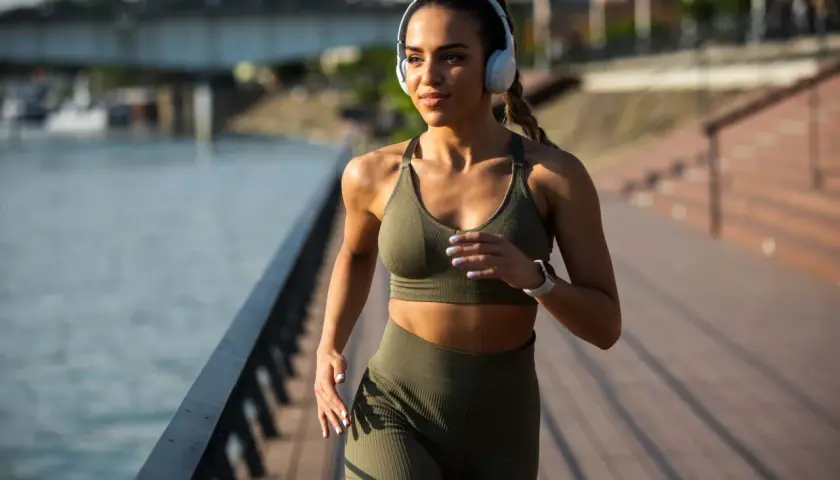 Frau mit Kopfhörern joggt am Wasser entlang. Nach 1 Monat Joggen sieht sie fit und energiegeladen aus.