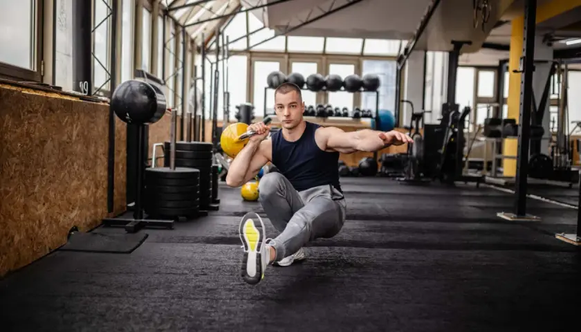 Mann macht einen Pistol Squat mit Kettlebell im Fitnessstudio.