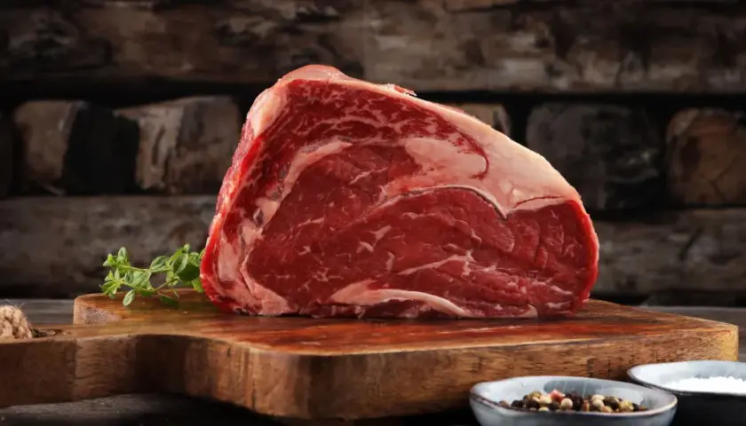 Ein saftiges Stück rotes Fleisch, reich an Eisen, liegt auf einem Holzbrett. Daneben Kräuter und Gewürze.