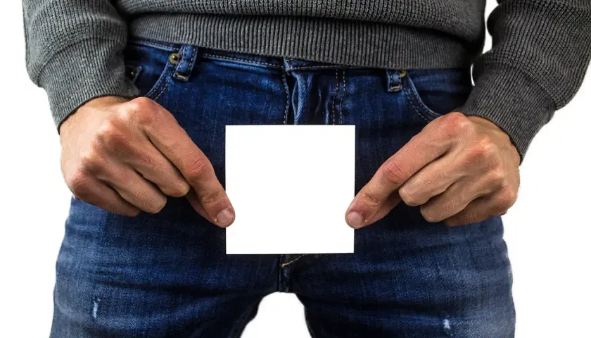 Mann hält ein weißes Blatt Papier vor sich, das eine Beule am Penis verdeckt.